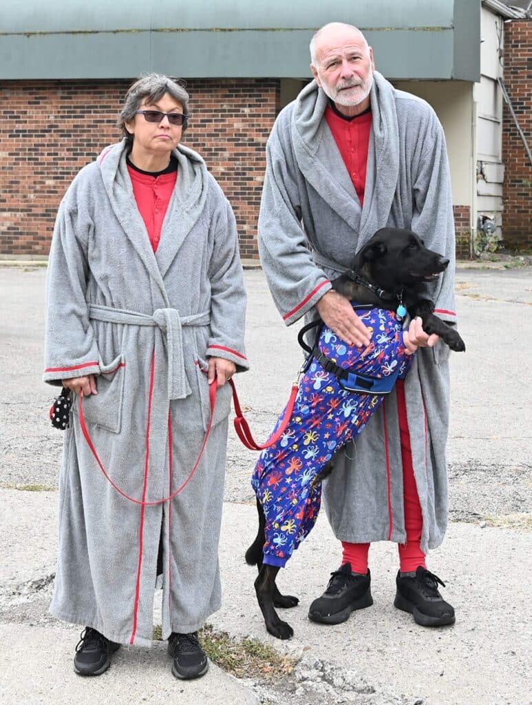 Two humans in bath robes with black dog in pajamas
